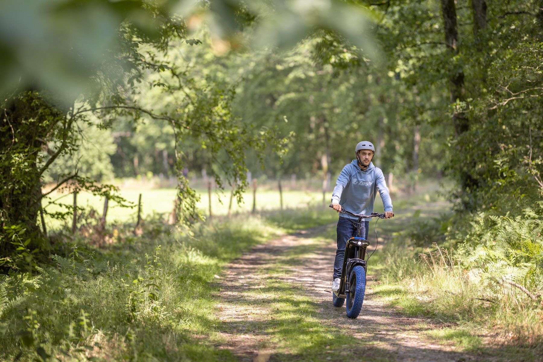 Homme roulant en trottinette électrique Zosh sur un sentier ombragé en forêt landaise