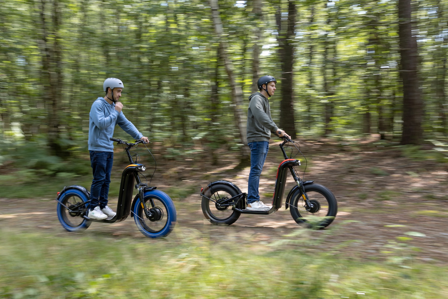 Deux hommes en balade sur des trottinettes électriques Zosh sur un chemin forestier, effet de vitesse